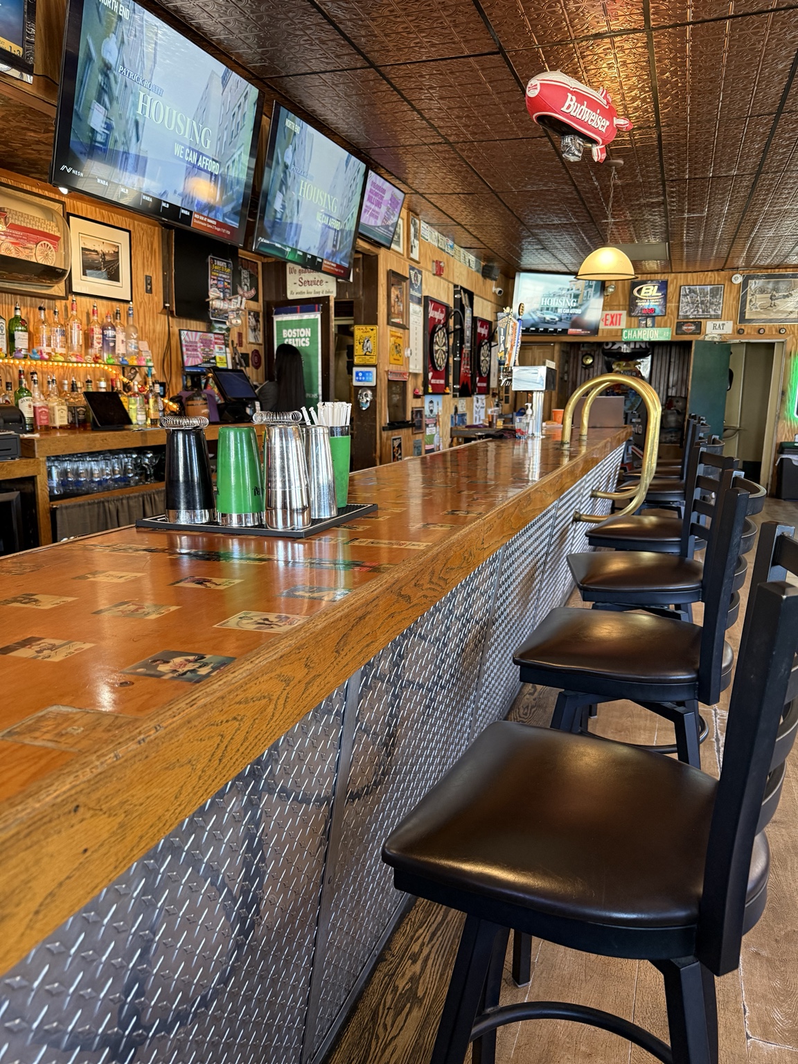 The wooden bar with sports memorabilia, illuminated signs, televisions, and a row of bar stools